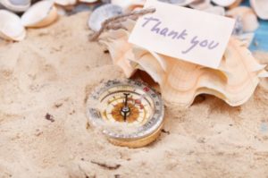 Seashell in the sand with compass and thank you note