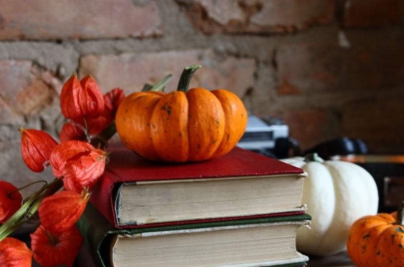 stack of books with pumpkins and fall foliage