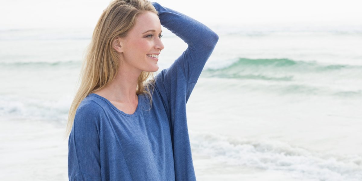 Side view of a smiling casual young woman standing at the beach